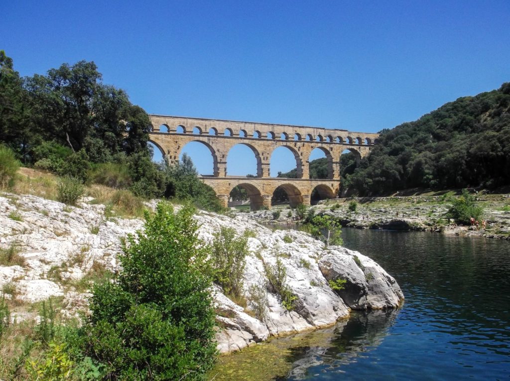 A river runs around a large rocky surface towards the Gardon Viaduct.