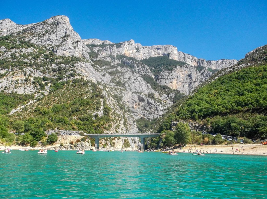 Creamy blue water flows through Verdon Gorge, France. Tourists on pedalos and kayaks happily sail along.