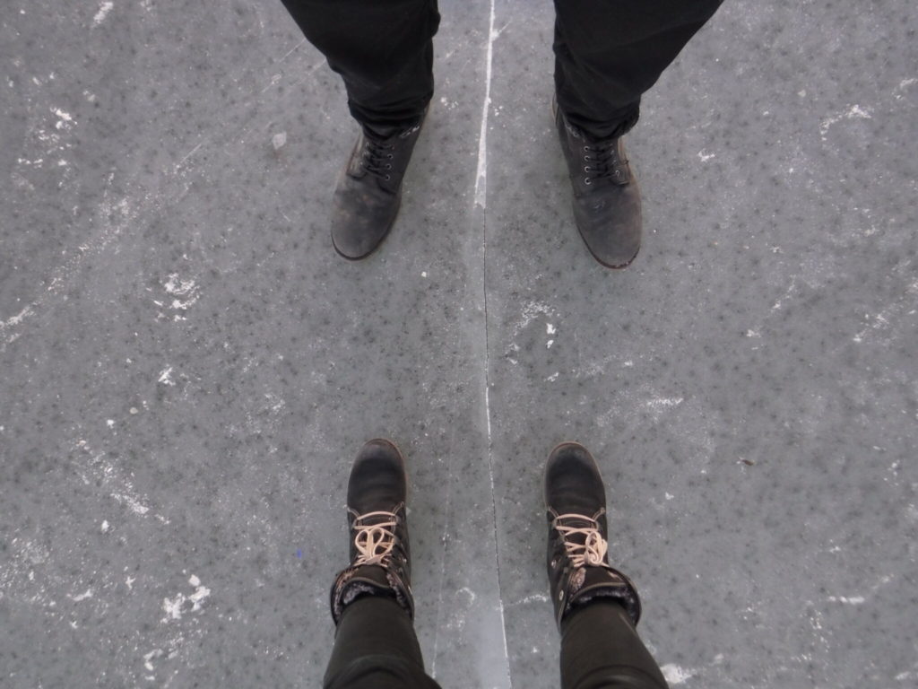 The boots of two people stood on a frozen lake.