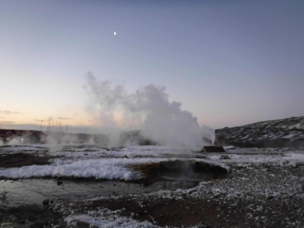Steam rises from a geysir as the moon comes into view.