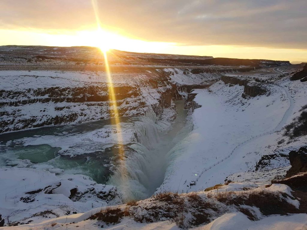 A huge crack in the earth reveals a frozen waterfall as the sun goes down over the mountains.