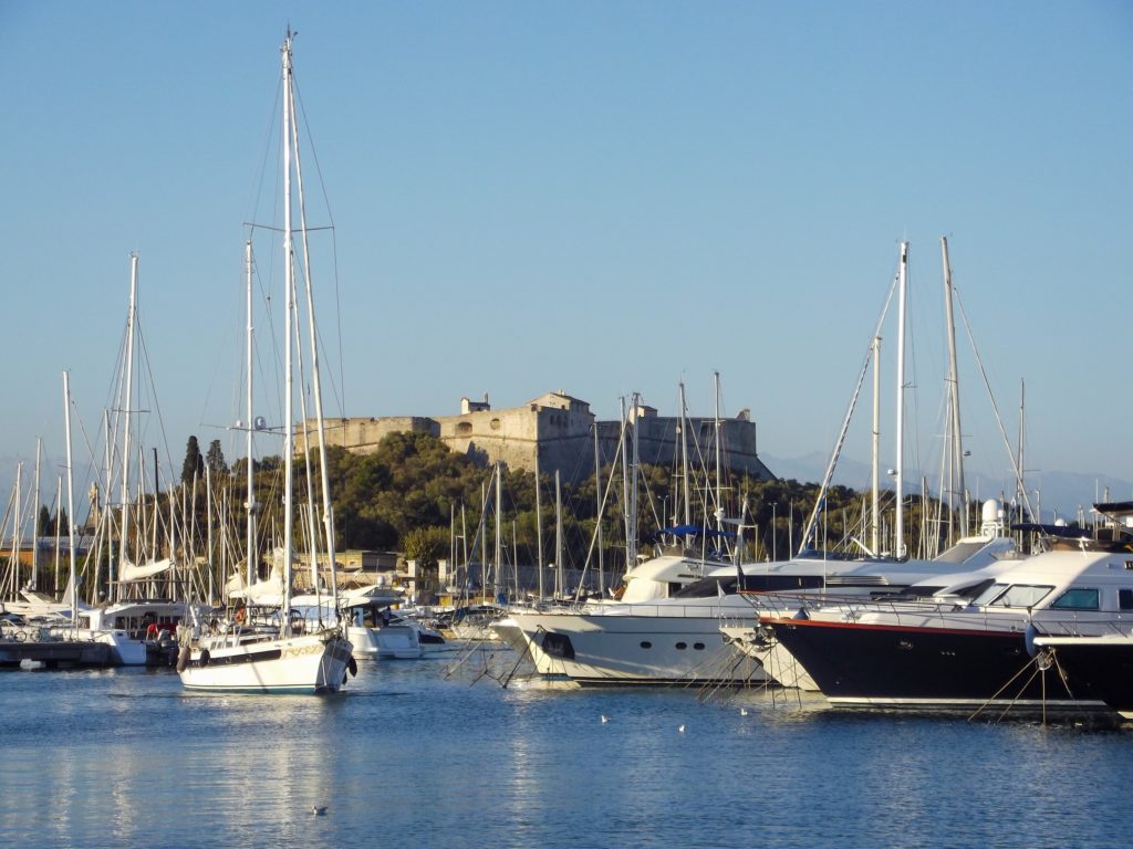 Boats in a French harbour. A large fort lies on the hill in the distance.