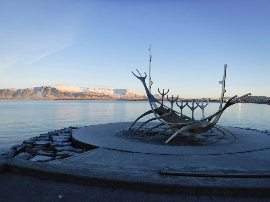 The famous Sun Voyager Sculpture stands on the coast opposite snow-covered mountains.