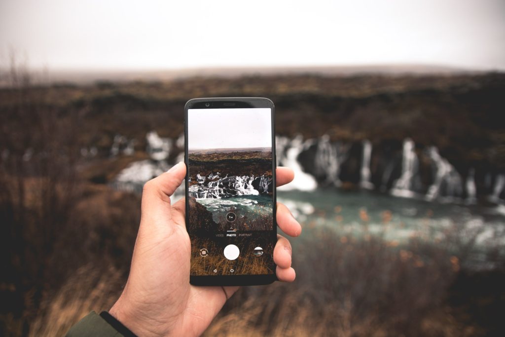 A person holds a phone, which displays a photo of a waterfall about to be taken.