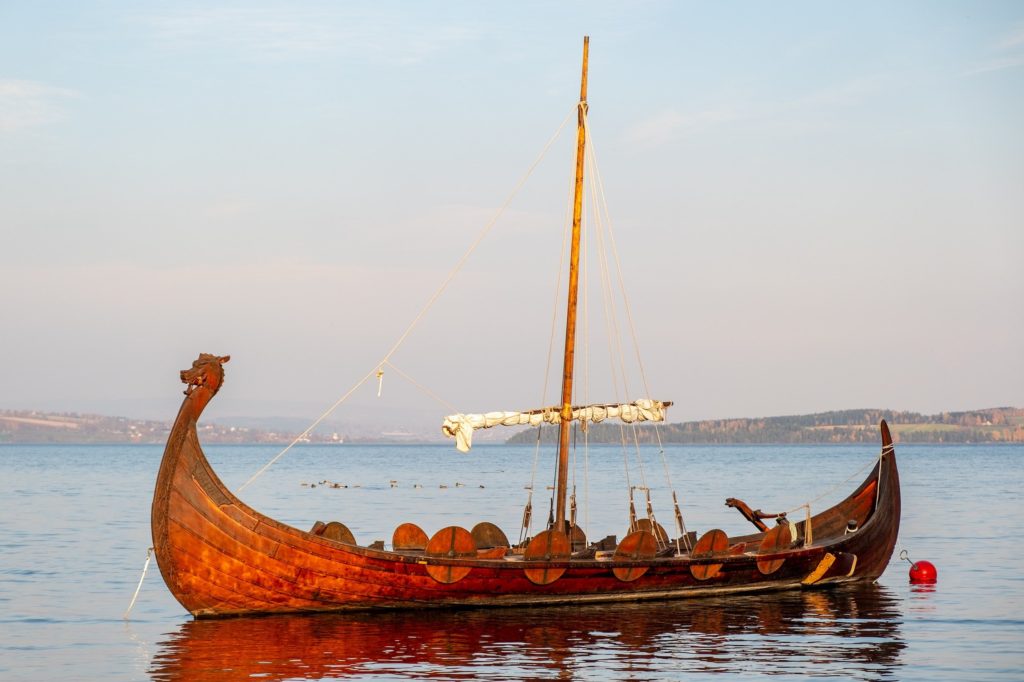 A traditional viking longship glides along the water in the sunshine.