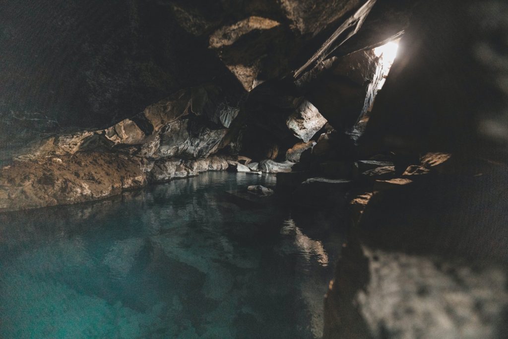 A cave with clear waters and a small window of sunshine coming in.