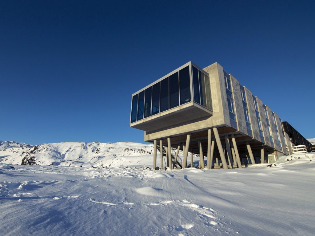 A rectangular box hotel stands on concrete stilts in the snow.