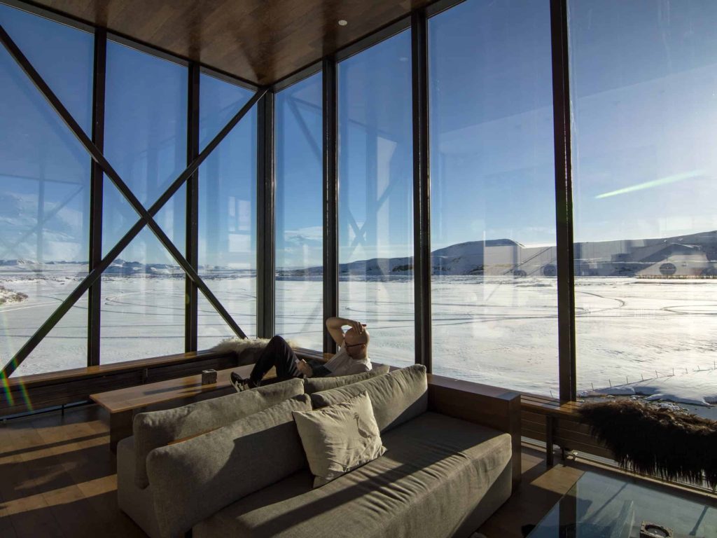 A man sits in a room of floor-to-ceiling windows which reveal a snowy landscape.