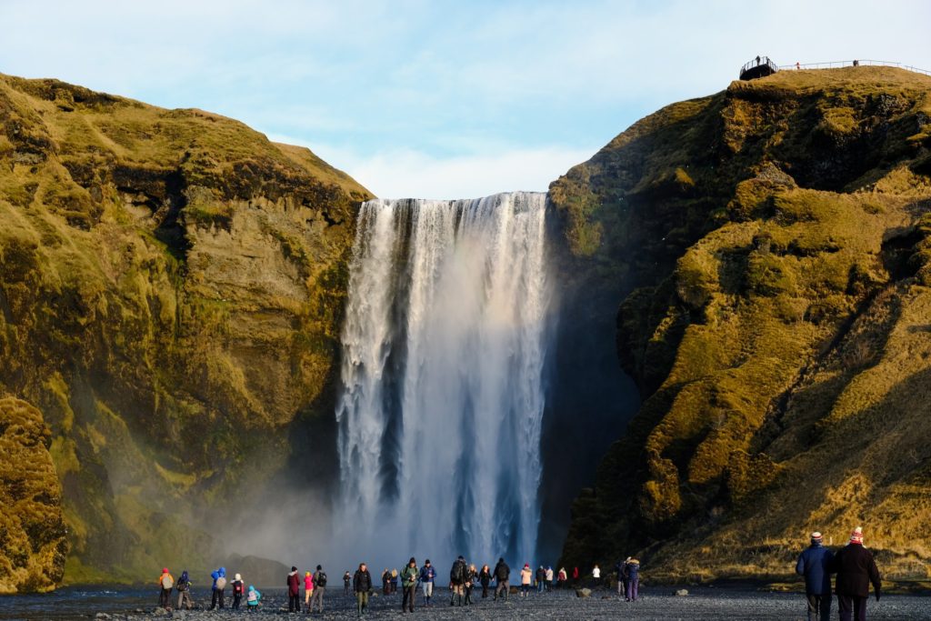 Water crashes down Skógafoss Waterfall. Several onlookers admire the view from the bottom.