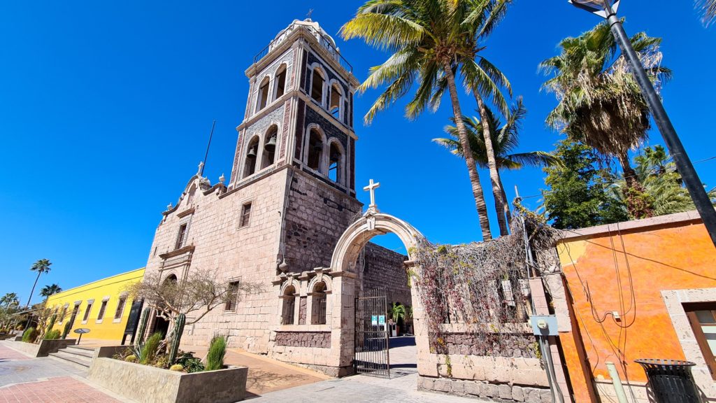 A small stone church with a bell tower stands in the Mexican sunshine.
