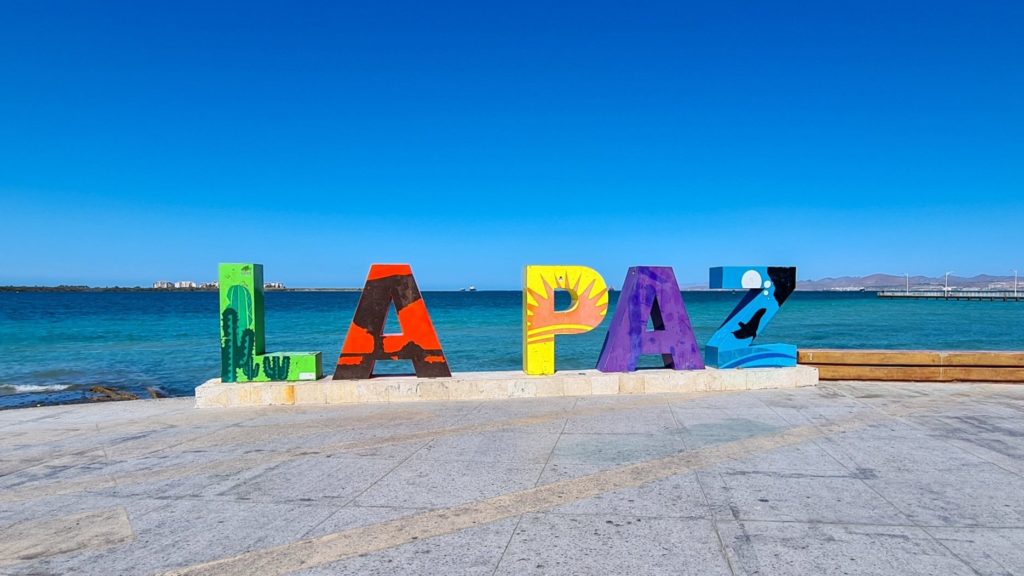 The La Paz sign is made up of multiple colours and backs onto the ocean.