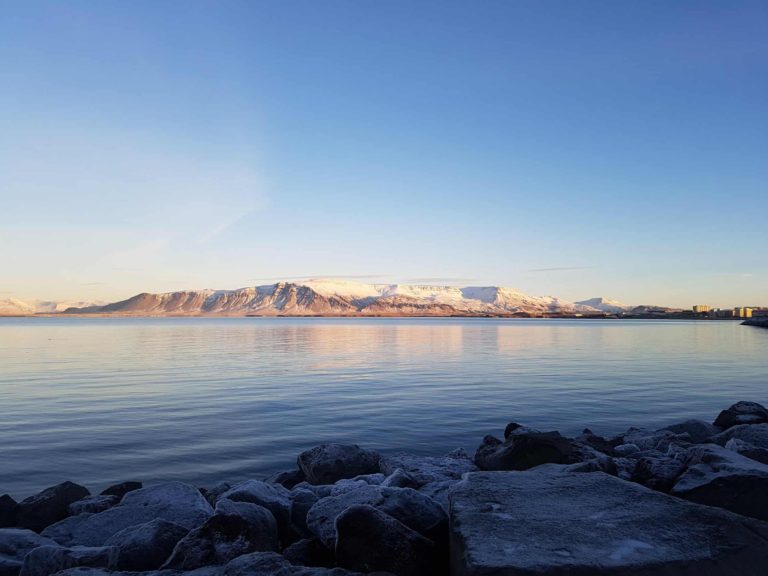 A view across the water to snowy mountains, golden in the morning sunshine.