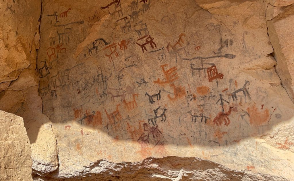 Red, orange and black figures have been painted onto a cave wall in Loreto. We can clearly see depictions of people and animals.