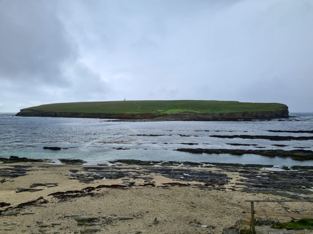 A small green island is cut off by the high tide. The pathway across is just visible underneath the shallow water.