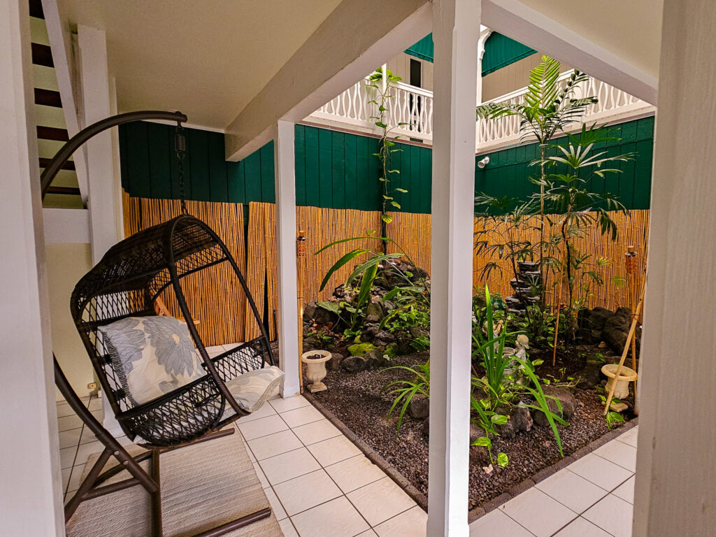 A hanging egg chair sits in front of a small open garden space.