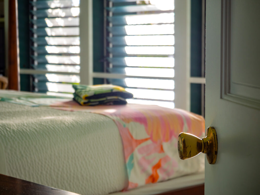 POV: You open a hotel room door to a bright white space with colourful blankets and towels.