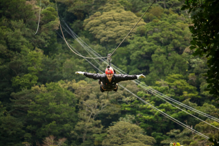Dan, lying on his front with his arms out either side, ziplines over thick rainforest.