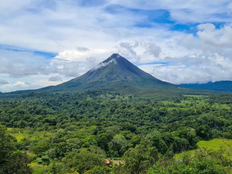 An unobstructed view of Arenal Volcano. The volcano and surrounding lands are a vibrant green and are covered with trees.