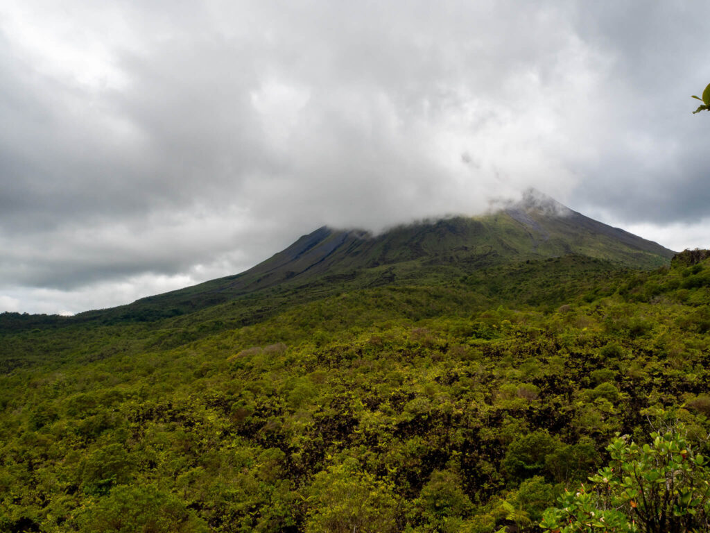 Grey clouds partially covering the impressive Arenal Volcano as seen from the hiking trail.