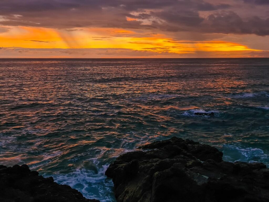 The sunset from a cliff's edge looking out to sea. In the distance, small patches of rain can be seen.