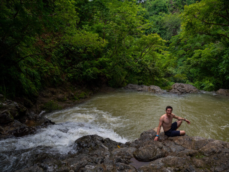 Dan sitting by a pool at the end of Montezuma Waterfall. He is smiling and looks ready for a swim.