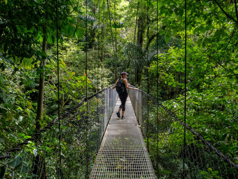 Lucy walking over a hanging bridge in Costa Rica. She is looking over the side to admire the view.