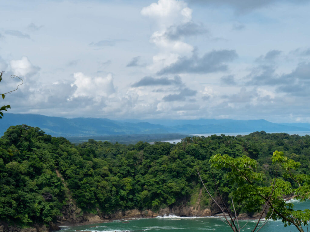 A tree-covered peninsula stretching out into the sea, and behind, a range of green mountains.