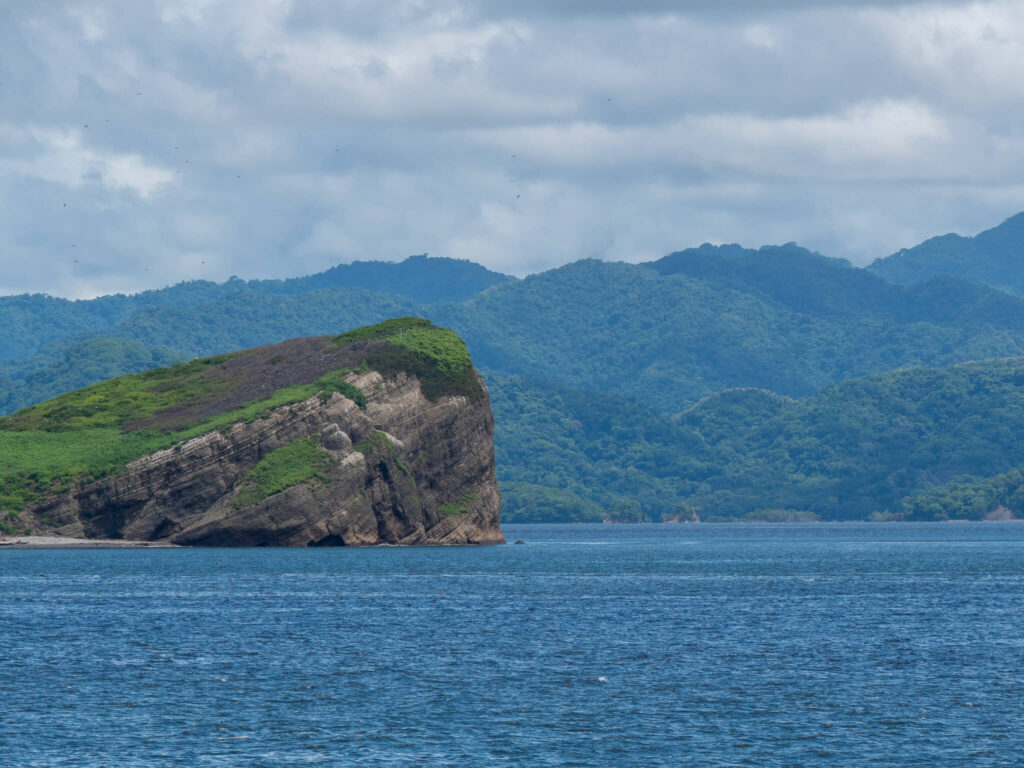 The Nicoya Peninsula in Costa Rica as viewed from a ferry. A rocky island stands out against the water.