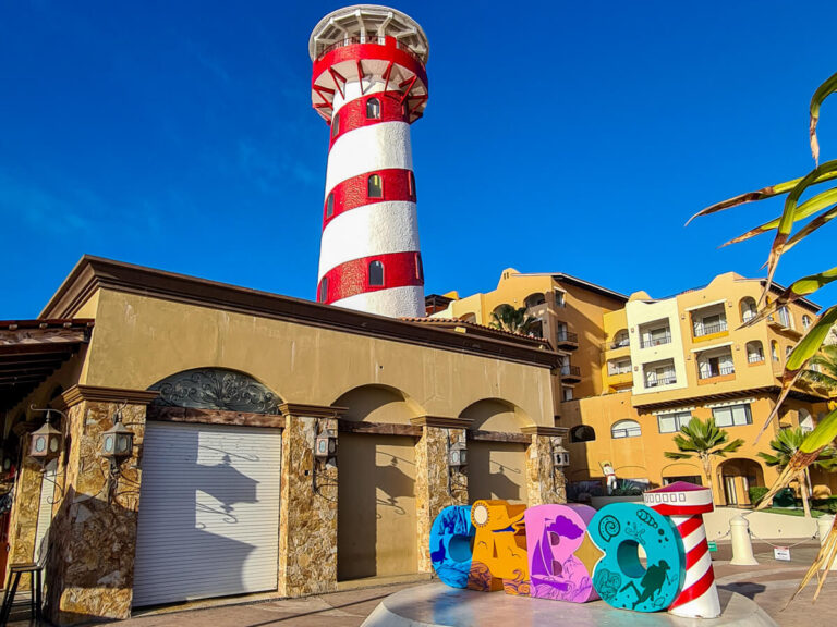 A striped lighthouse behind the bright and colourful Cabo sign.