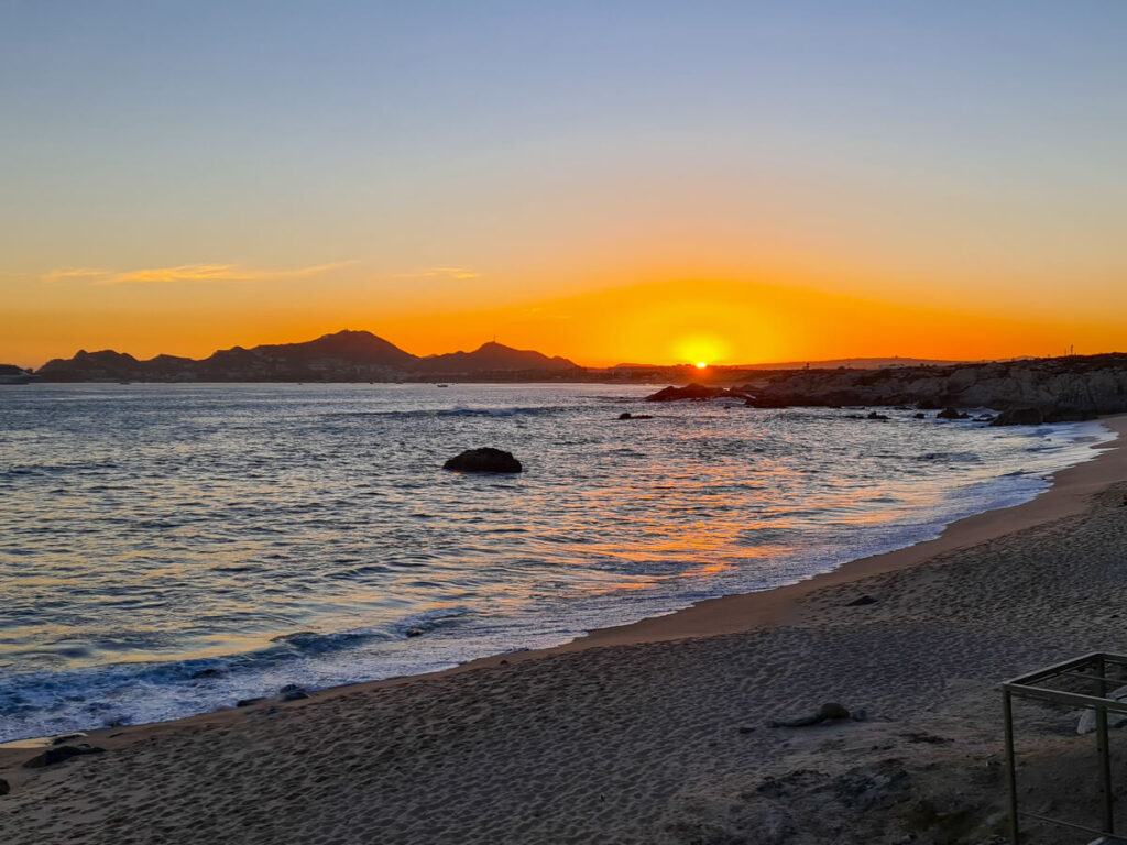 The sun setting behind the mountains of Chileno Bay. The beach is completely empty and the water is calm.