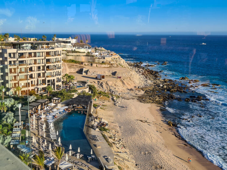 An aerial view of The Cape (a Thompson Hotel). A long swimming pool separates the many hotel rooms from the quiet beach below.