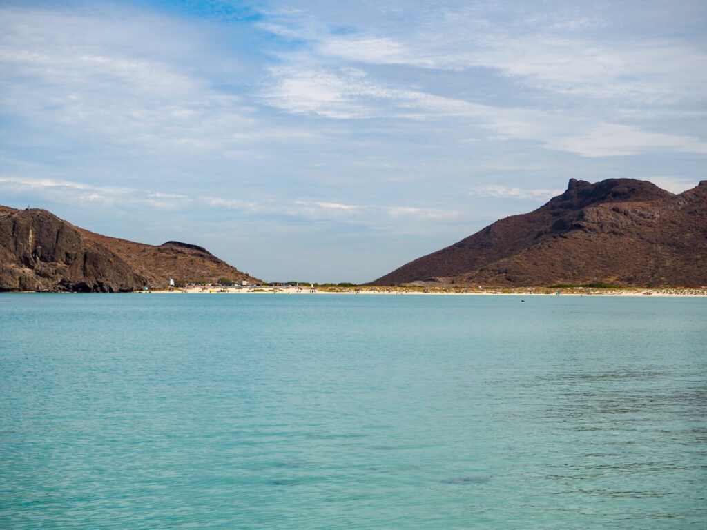 Balandra Beach from a distance away. Red-brown hills are flanking the beach on each side.