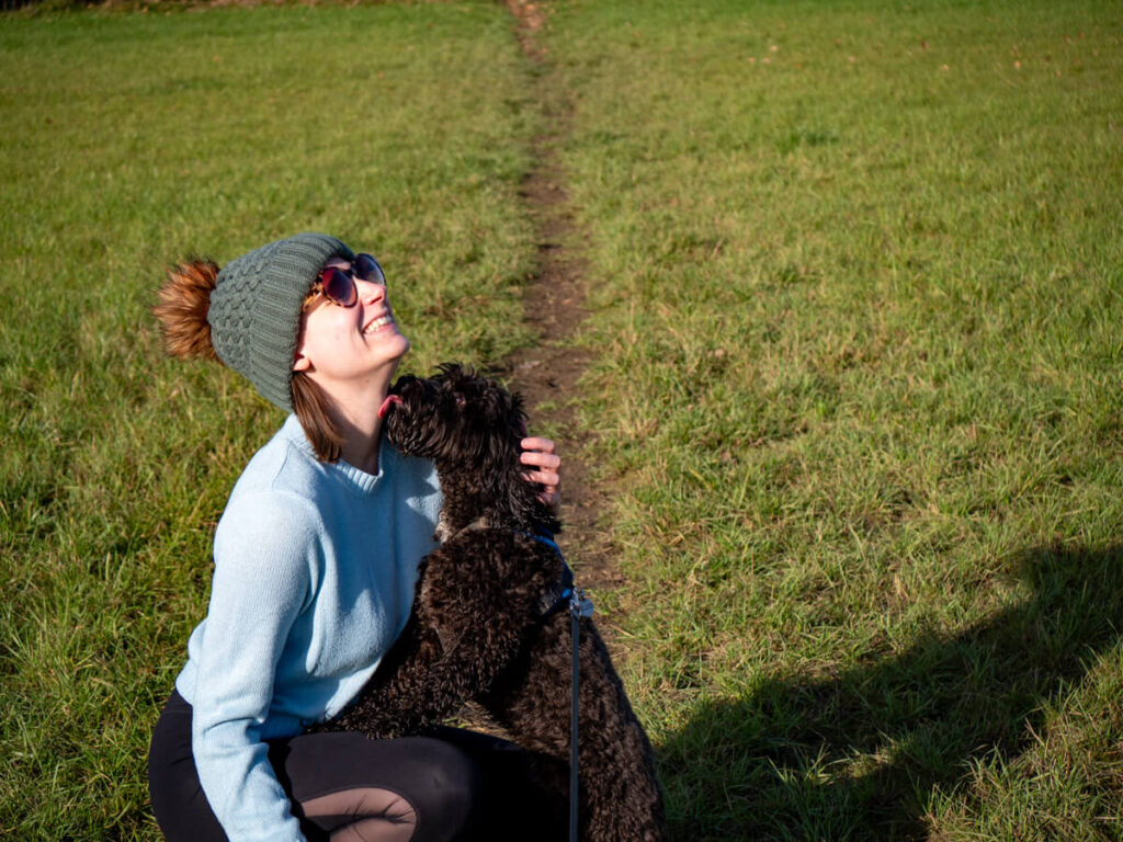 A happy dog jumping up to lick Lucy's neck as she laughs in the afternoon sunshine.