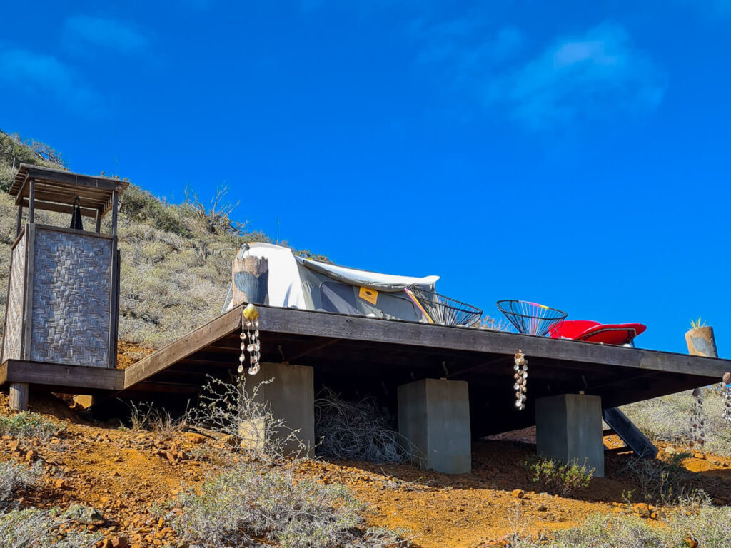 One of campsites at Magdalena Bay Whales Camp. A glamping tent, outdoor shower and seating area are on a raised wooden platform looking out to sea.