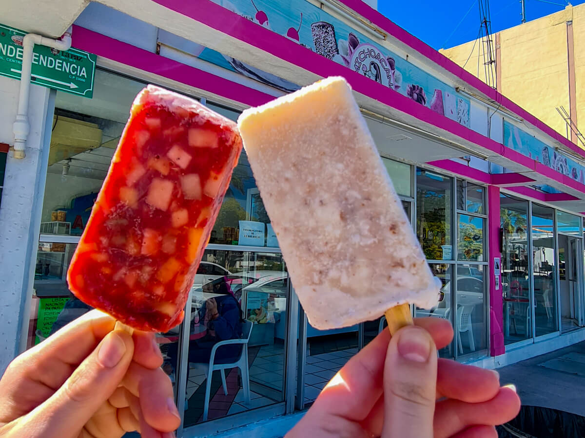 Dan and Lucy holding up their ice lollies. One is red (chilli-flavour) with small frozen pieces of fruit inside, the other is white (coconut flavour).