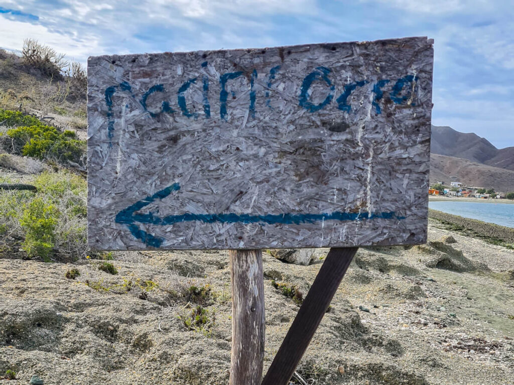 A sign reading "Pacific Ocean" and an arrow pointing to the left marks the start of a hiking trail on Isla Magdalena.