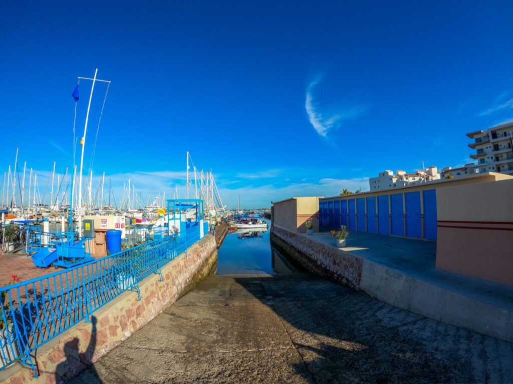 A ramp slopes down into La Paz Marina. In the distance, many boats are anchored in the rows of piers.