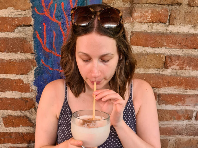 Lucy sipping on a large Pina Colada through a straw. Her hair is curly and she has sunglasses resting on her head.