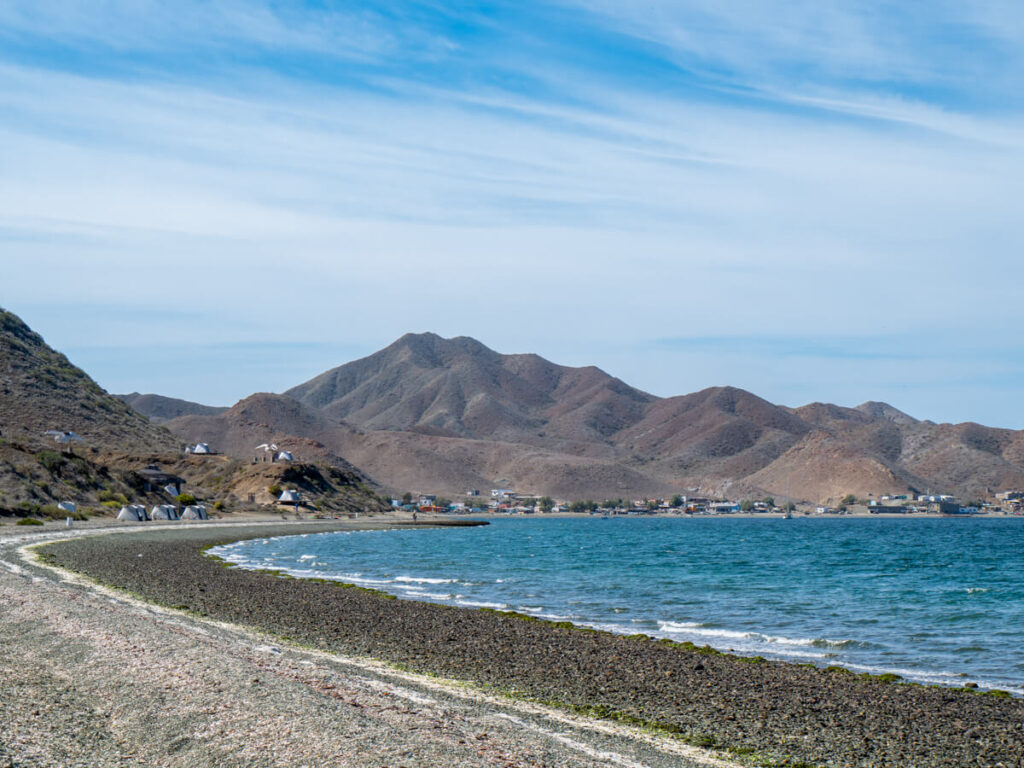 Magdalena Bay Whales Camp as viewed from the edge of the beach. To the right of the campground lies the small town of Magdalena Bay which backs onto grey-brown mountains.