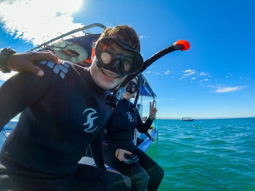 Dan and Lucy sitting on the edge of a small boat in wetsuits and dive masks on a whale shark tour in La Paz.