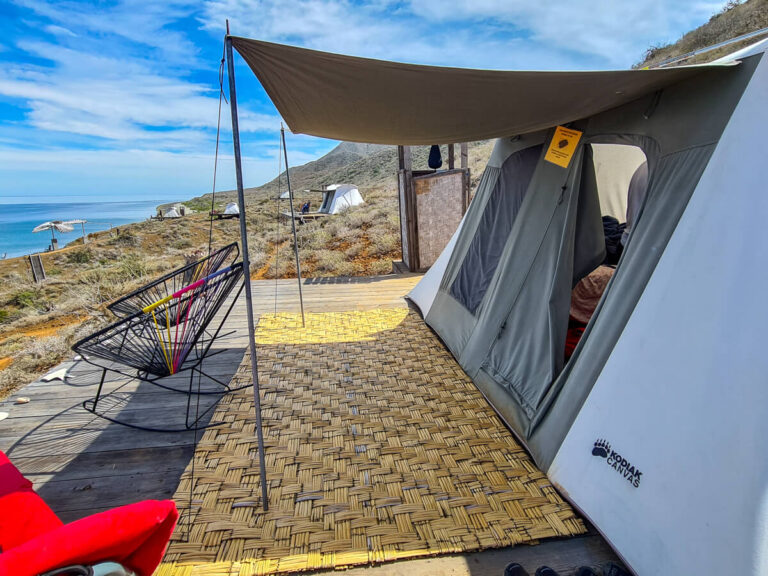 The view from a glamping tent at Magdalena Bay Whales Camp. The hills slope down to a beach and then to calm waters.