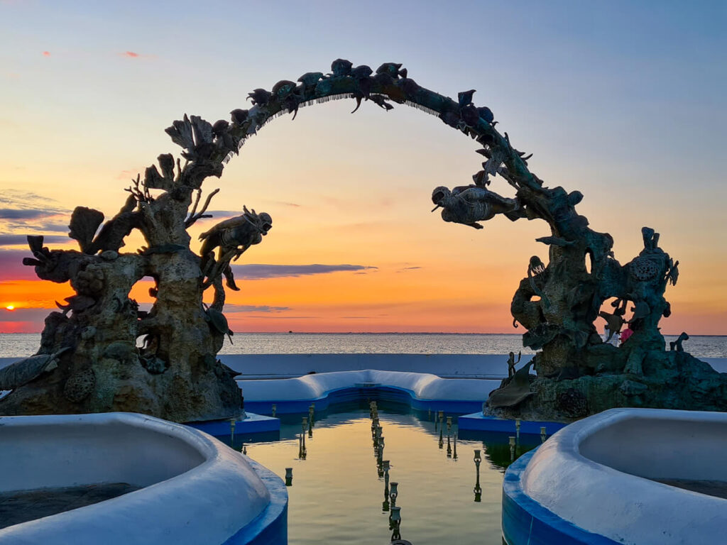 A bright orange sunset behind an arch representing coral on the malecĂłn in Cozumel.