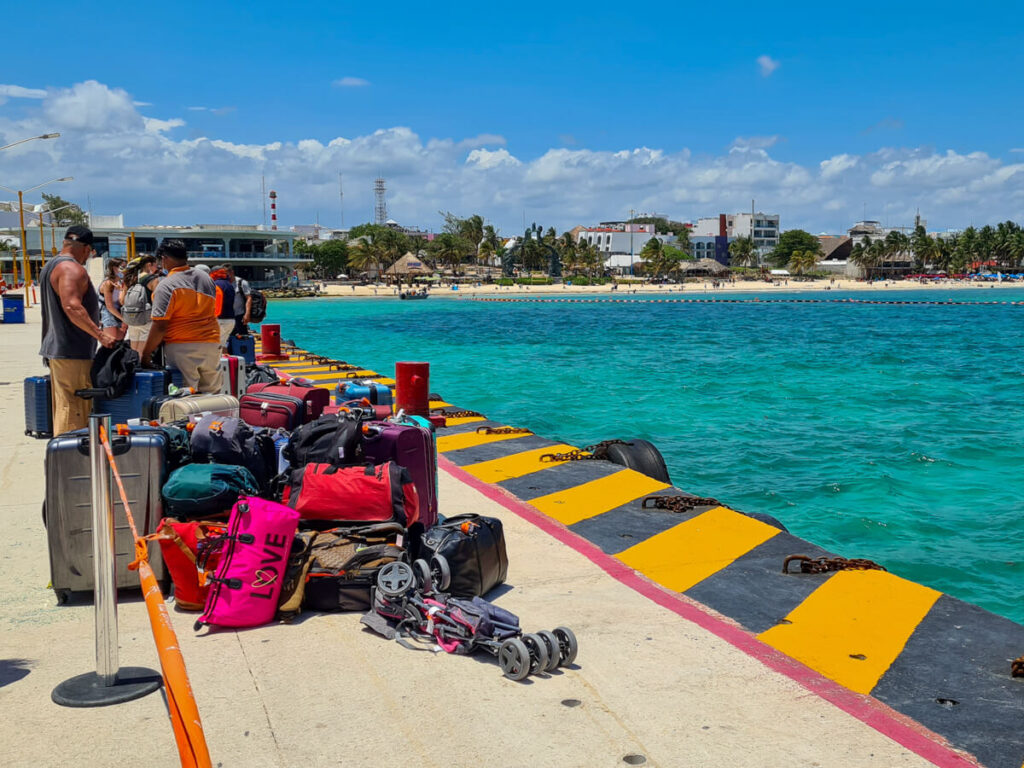 A collection of luggage on the concrete Cozumel Ferry dock, backed by bright blue sea in Playa del Carmen.