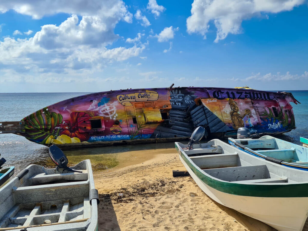 A colourful boat covered in graffiti art on a beach off the malecĂłn in Cozumel.