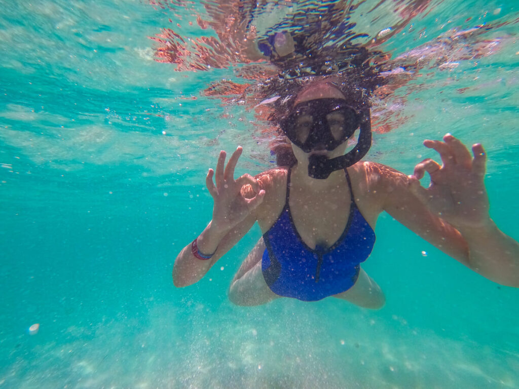 Lucy snorkelling in clear blue water, making "OK" symbols with her fingers.