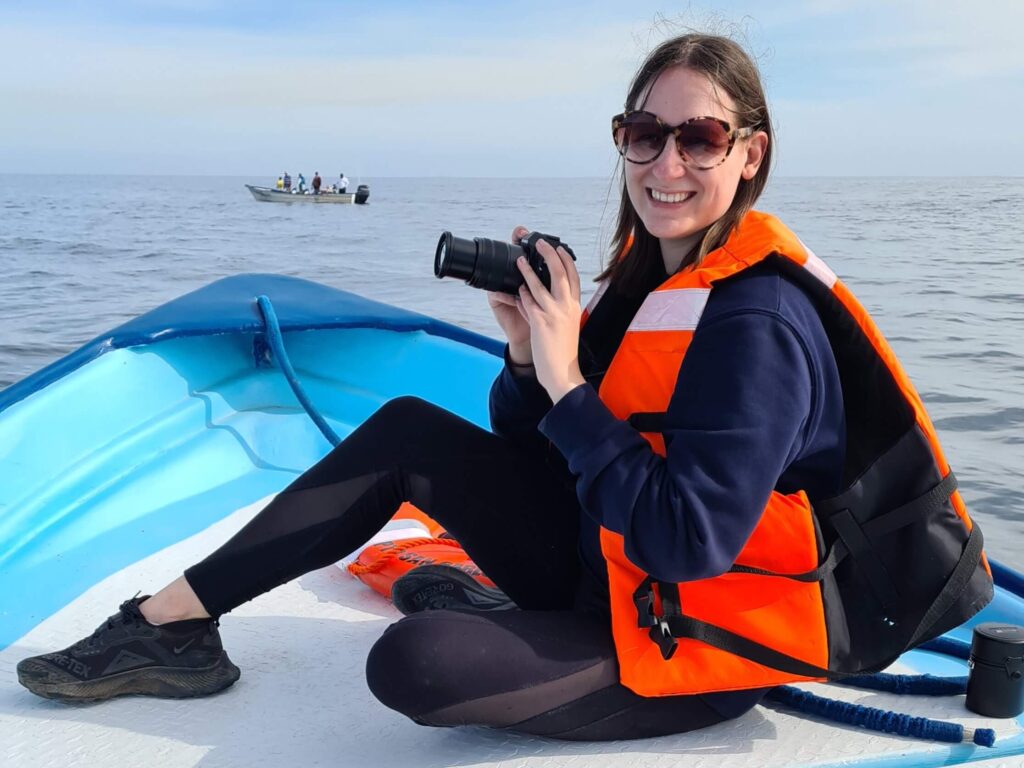 Lucy sitting on the front of a panga, wearing a life jacket and holding a camera, whale watching in Magdalena Bay.