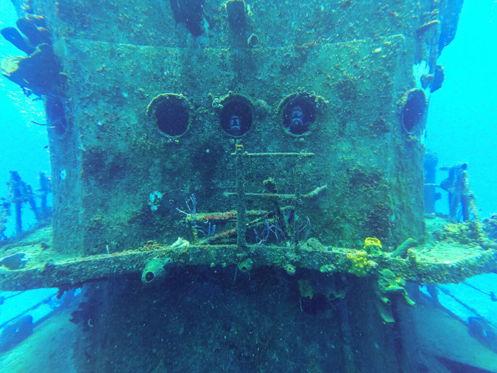 Lucy and Dan poking their heads through the portal windows of a shipwreck while SCUBA diving in Cozumel.