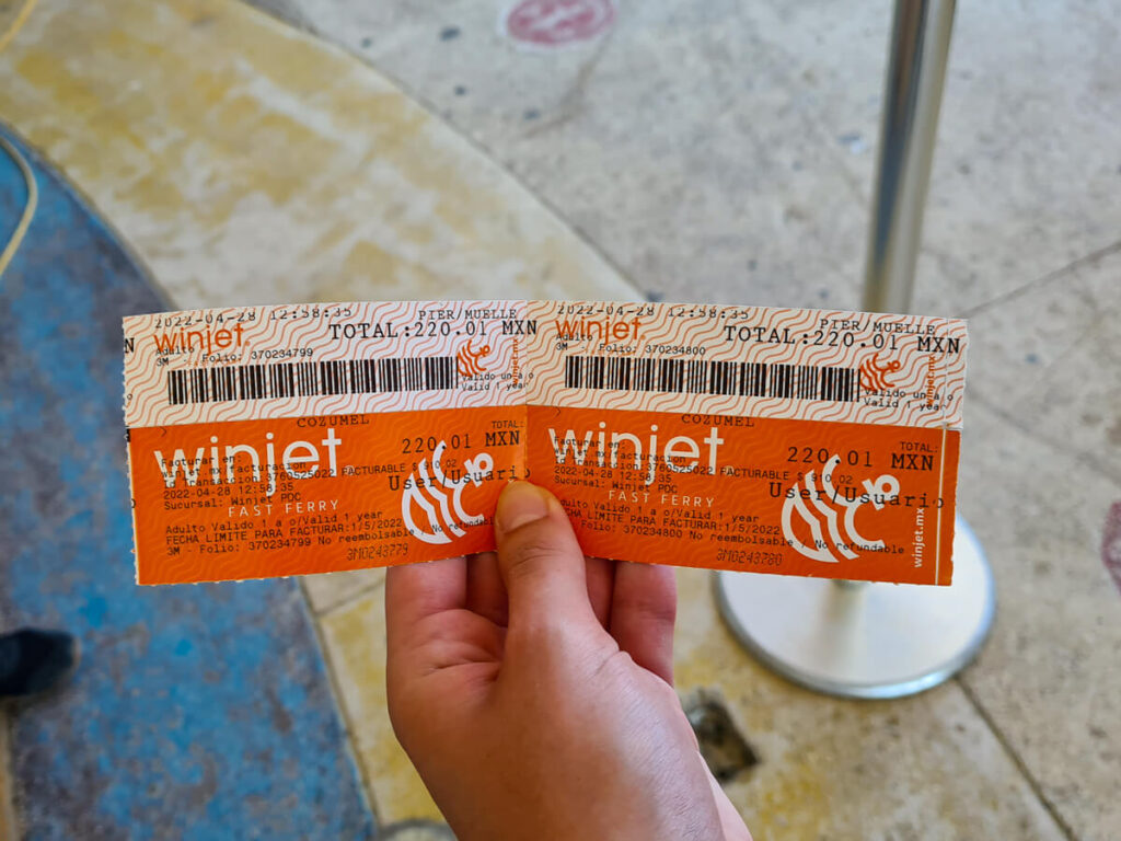 A hand holding two tickets for the Cozumel Ferry in the terminal building.