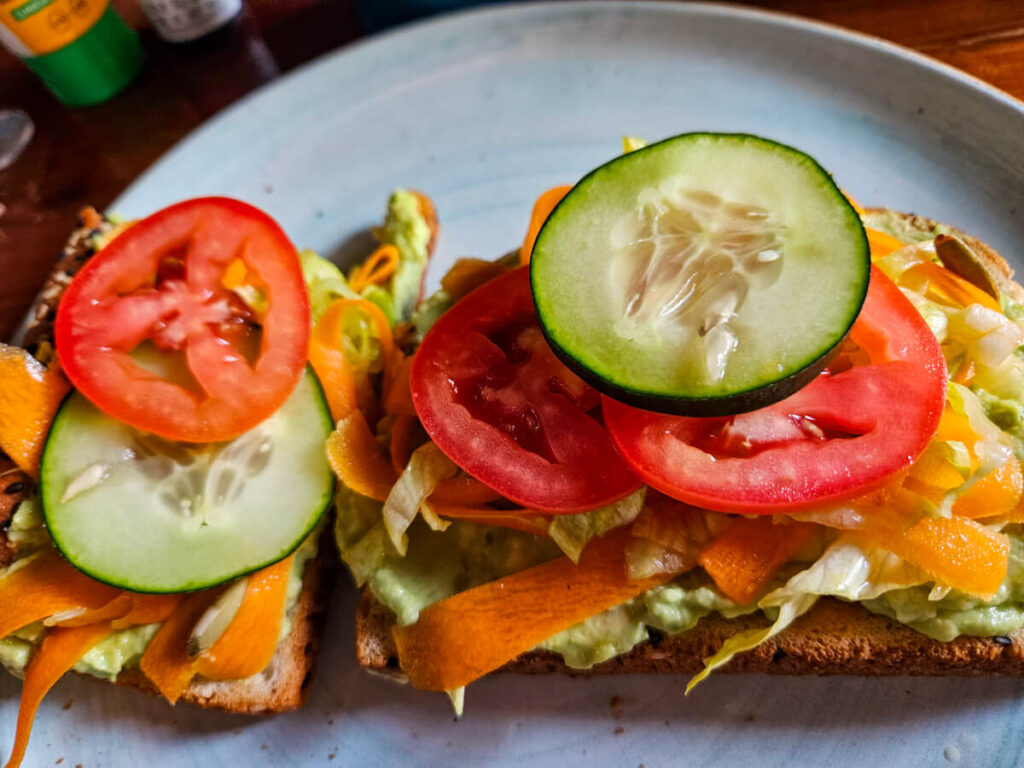 A plate of avocado toast topped with lettuce, carrot, tomato and cucumber.