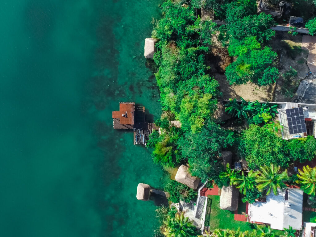 A section of Bacalar Lagoon as viewed from a drone. The water is a blue-green colour and matches well with the surrounding greenery. Lucy and Dan are relaxing on a wooden dock.